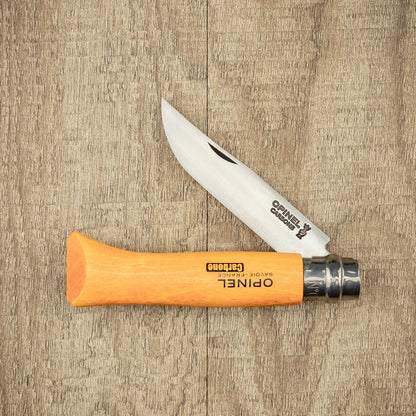Opinel Carbon No.08 Folding Knife with a beech-wood handle and open carbon-steel blade, showcasing timeless design and craftsmanship on a wood-grain surface.