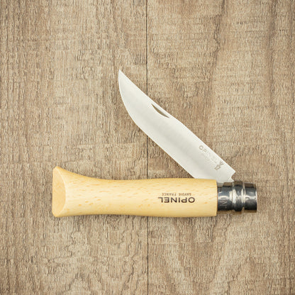 Opinel Inox No.09 Folding Knife with stainless steel blade and light wooden handle, open on a wooden surface, showcasing its iconic ring-lock collar.