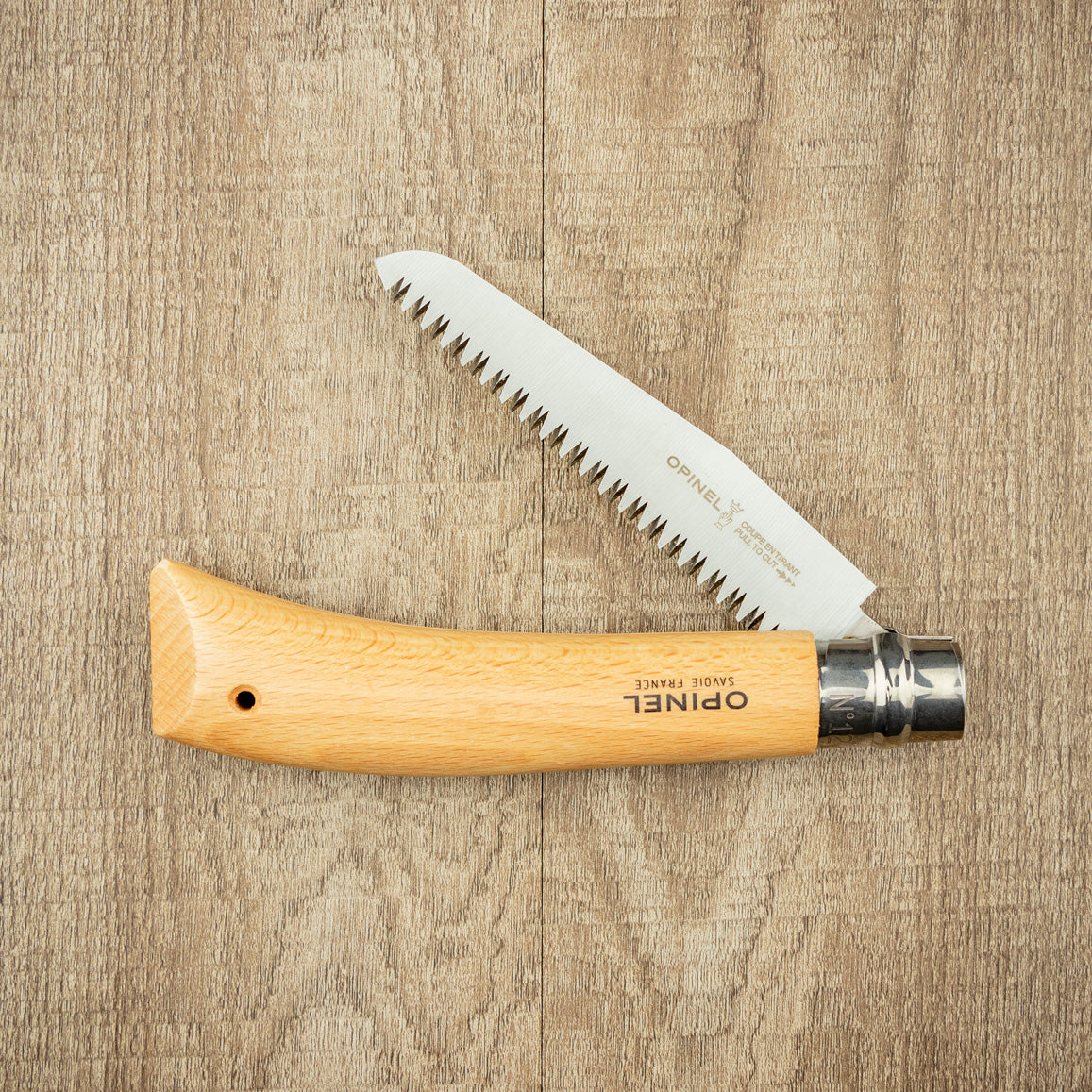 Opinel Folding Saw with serrated stainless-steel blade and beech-wood handle, ideal for trail clearing and tree de-limbing, displayed on wood surface.