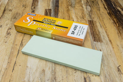 Naniwa Specialty/Super Stone 10000 210x70x10mm on a wooden table beside its orange SP-490 box, ideal for achieving precise, professional-grade sharpening.