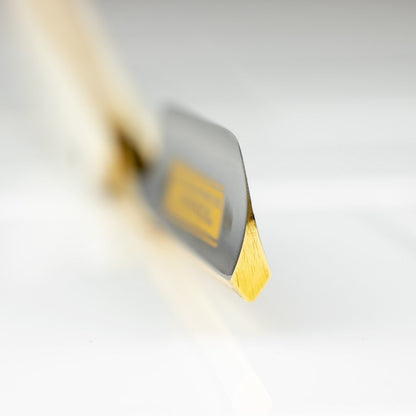 Close-up of Dovo Bismarck Straight Razor 6/8” blade, highlighting its gold-shaded bevel on a white surface, wooden handle softly blurred in the background.