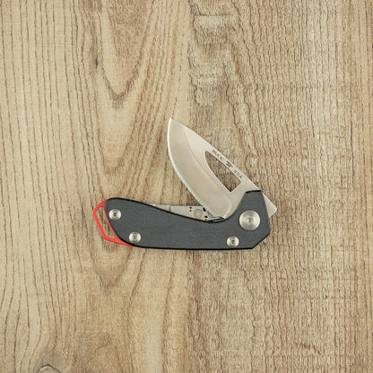 Buck Budgie Folding Knife with stainless-steel blade and black handle, partially opened on a light wood surface, showcasing its modern, durable design for everyday carry.