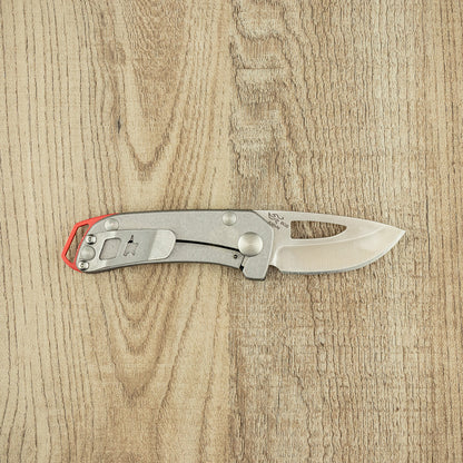 Buck Budgie Folding Knife on wood surface, featuring a satin-finished steel handle with pocket clip and partially open drop-point blade. Ideal for reliable everyday carry.