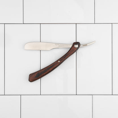 Feather Artist Club DX Folding Handle Shaving Razor with a wooden handle and stainless-steel blade, open against a white tile background, showcasing its classic design.