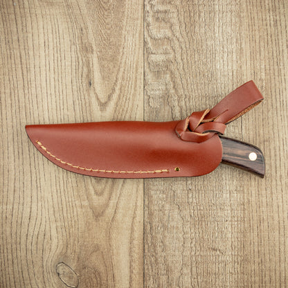 Grohmann #104F Flat Grind Mini Skinner with rosewood handle in a brown leather sheath on a light wood surface, ideal for precise control in hunting.