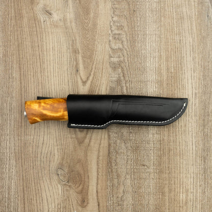 Helle Knives Eggen 100mm Hunting Knife sheathed in black leather, featuring a light wooden handle, rests on a wooden surface, epitomizing craftsmanship and durability for outdoor use.