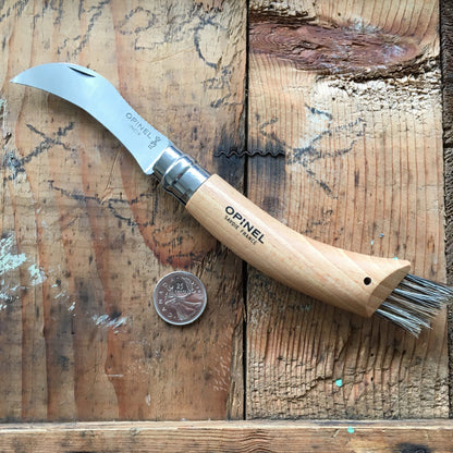 Mushroom Hunter Bundle: Opinel mushroom knife with curved blade and handle brush on wooden surface, beside a Canadian quarter for scale.