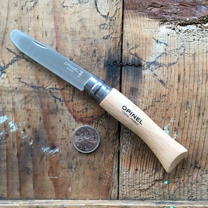 Opinel Inox No.07 Kids Safety Folding Knife with stainless blade and beechwood handle, open beside a Canadian quarter on a textured wooden surface.