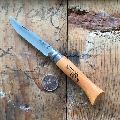 Opinel Carbon No.06 Folding Knife with carbon-steel blade and corkscrew on wooden surface, shown with Canadian quarter for scale.