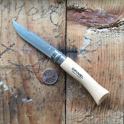 Opinel Inox No.07 Folding Knife with stainless steel blade and beechwood handle, shown open beside a Canadian quarter for scale on a wooden surface.