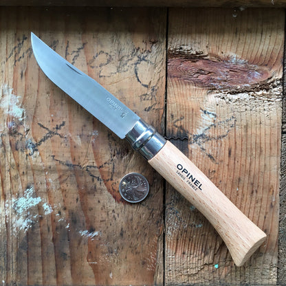 Opinel Inox No.09 Folding Knife with stainless-steel blade and beechwood handle, displayed open on a wooden board beside a Canadian quarter for scale.