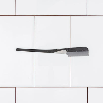Iwasaki Kamisori straight razor on white tiles, showcasing its handcrafted carbon steel blade and ergonomic design, suitable for precise shaving.