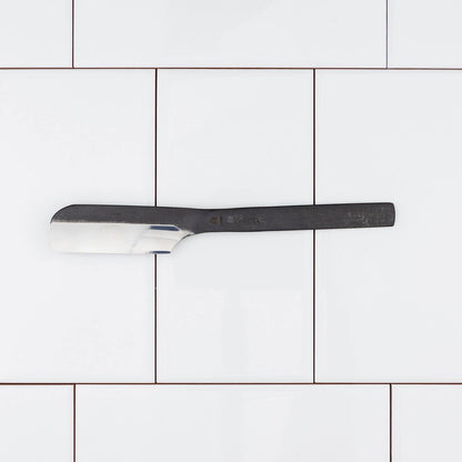 Takami Kamisori Japanese Straight Razor with Western Grind, displayed on a white tile backdrop, showcasing its precise single-bevel blade design for accessible, traditional shaving.