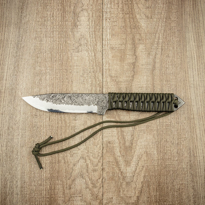 Seki Kanetsune KARASU Outdoor Knife 125mm with a hand-forged blade and paracord-wrapped handle, laid on wood, epitomizing durability and precision.