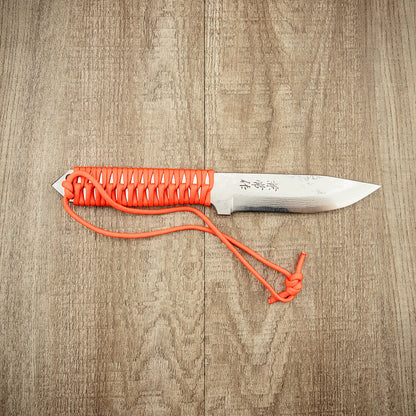 Seki Kanetsune SHU-KARASU Outdoor Knife 125mm with paracord-wrapped handle, etched blade, ideal for survival tasks, lies on a wood-grain surface.