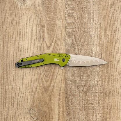 Kershaw Dividend folding knife with an olive-green aluminum handle and partially serrated stainless steel blade on a light oak surface.