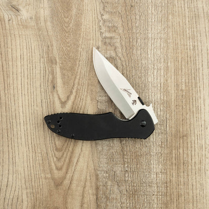 Kershaw Emerson CQC-6K D2 folding pocket knife with a black handle and satin-finished blade, half-open on a light wood surface.
