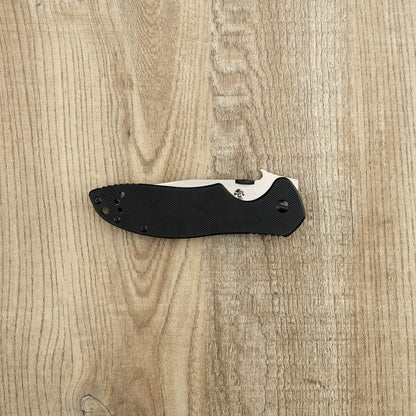 Kershaw Emerson CQC-6K D2 pocket knife with a black textured handle and partially exposed stainless-steel blade on a light wood-grain surface.