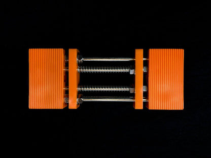 Stone Holder Spring Loaded: A compact clamp with orange plastic jaws and metal rods, designed for easy, secure stone holding without manual screw adjustments.
