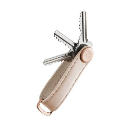 Orbitkey Leather Key Organizer with beige sleeve, fanning metal keys from a central pivot, featuring a D-ring for attaching larger items.