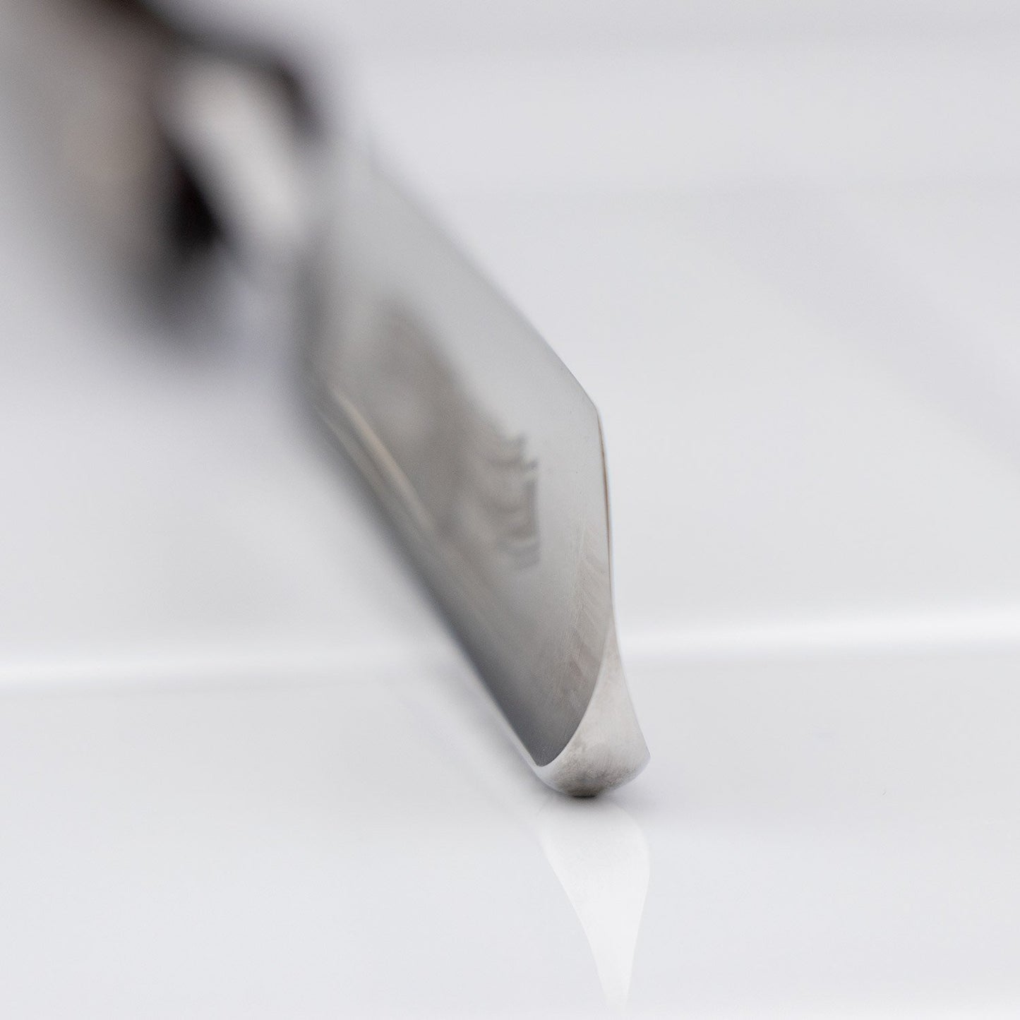 Ralf Aust Round Point 5/8 Straight Razor's polished blade tip rests on a glossy surface, highlighting its precision-crafted Solingen steel edge.