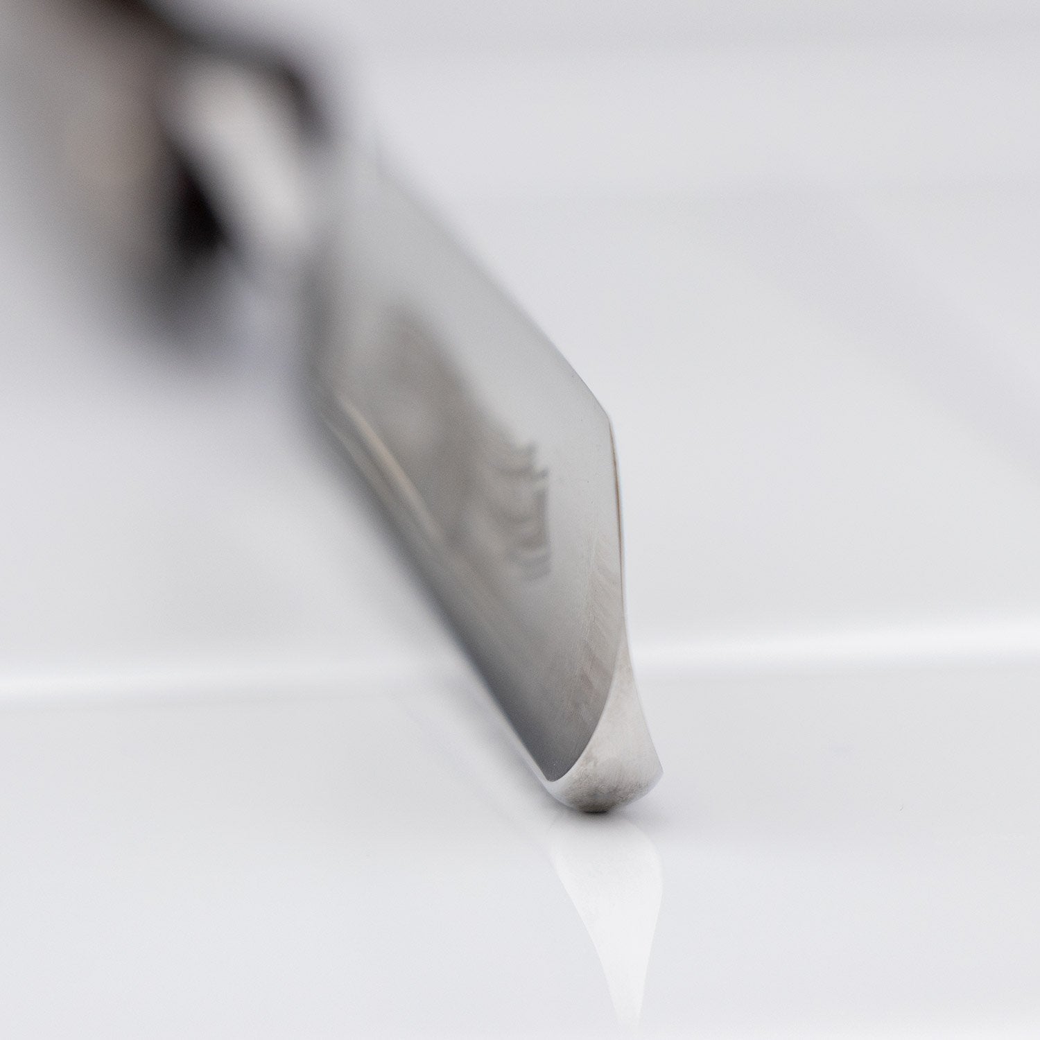 Ralf Aust Round Point 5/8 Straight Razor's polished blade tip rests on a glossy surface, highlighting its precision-crafted Solingen steel edge.