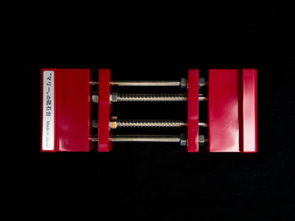 Stone Holder Spring Loaded in red, designed for securing stones effortlessly. Features two red plastic blocks with Japanese label, connected by steel rods and nuts. Made in Japan.