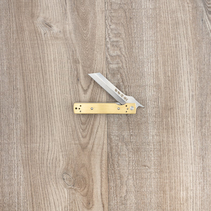 Seki Kanetsune Tanzaku-Tou Folding Knife 72mm with brass handle and tanto-style blade, displayed open on a wood surface, showcasing its precision craftsmanship.
