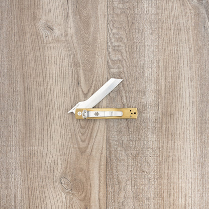 Seki Kanetsune Tanzaku-Tou Folding Knife 72mm with brass handle and stainless blade, laid open on wood grain surface, featuring a repositionable pocket clip.
