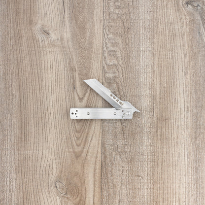 Seki Kanetsune Tanzaku-Tou Folding Knife 72mm, a Japanese-style friction folder, partly open on wood, featuring decorative Japanese characters etched into the blade.