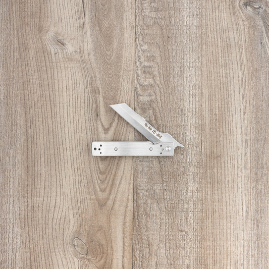Seki Kanetsune Tanzaku-Tou Folding Knife 72mm, a Japanese-style friction folder, partly open on wood, featuring decorative Japanese characters etched into the blade.