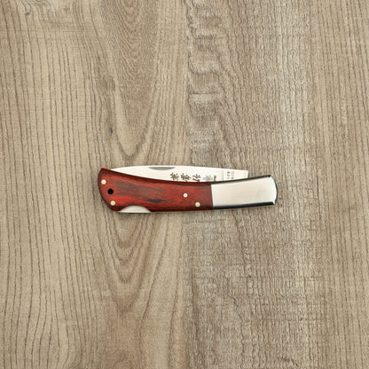 Seki Kanetsune Kaico-Tou Classic Folding Knife 70mm with a reddish Pakka wood handle and stainless-steel bolsters, partially exposed blade showing etched markings.