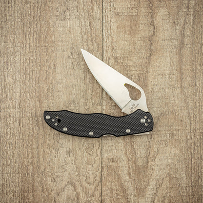 Spyderco Byrd Harrier 2 G10 folding knife on wood, featuring a stainless-steel blade with thumb-hole and textured G-10 handle with visible rivets, ideal for everyday carry.