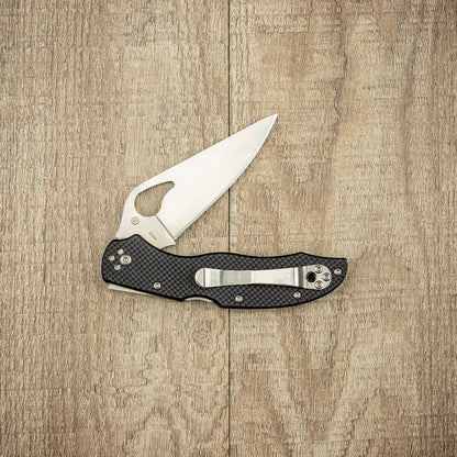 Spyderco Byrd Harrier 2 G10 folding pocket knife with a stainless-steel blade, thumb-hole for ambidextrous opening, and textured handle, laid open on wood.