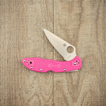 Spyderco Delica 4 Lightweight Pink S30V Folding Knife on wood, featuring a pink textured handle and satin-finished blade with Spyderco's round thumb-hole and logo.