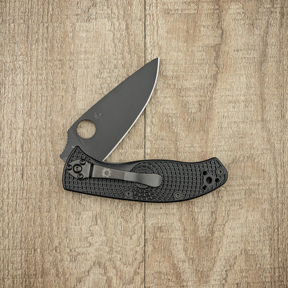Spyderco Tenacious Lightweight Black Folding Knife with textured handle and partially opened blade, laid on a wooden surface, showcasing its sleek design and functionality.