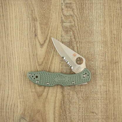 Spyderco Delica 4 folding knife with half-serrated VG10 stainless blade and sage-green FRN handle, open on wooden surface, showcasing lightweight, durable design.