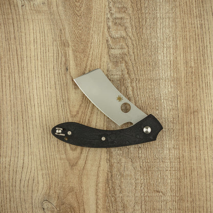 Spyderco ROC G10 pocket knife with a cleaver-style blade, featuring a distinctive thumb-hole opener and textured black handle, partially opened on a wooden surface.