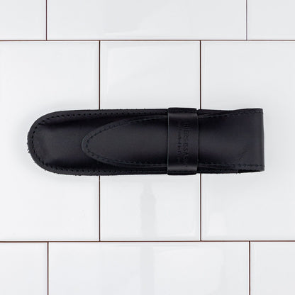 Top-down view of a Thiers Issard Straight Razor in a black leather pouch, highlighting its Spartacus design with red stamina wood scales.