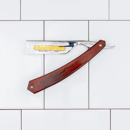 Thiers Issard Straight Razor, Spartacus, with a polished steel blade and red stamina wood handle, showcased on a white tiled background, embodying classic shaving precision and durability.